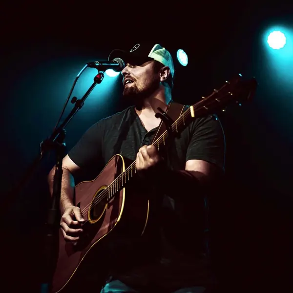 Jordan Beem singing and playing acoustic guitar under blue stage lights