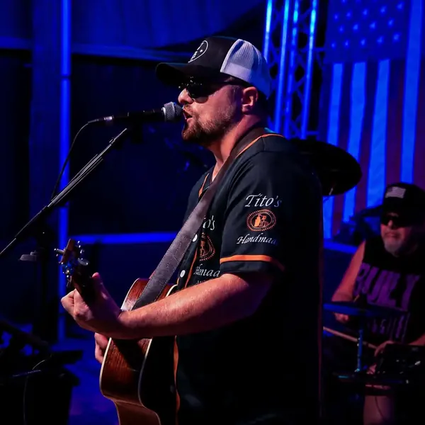 Jordan Beem on acoustic guitar with drummer Johnny G and an American flag behind the stage