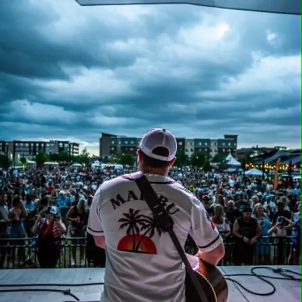 Jordan Beem on stage facing a big outdoor crowd under storm clouds