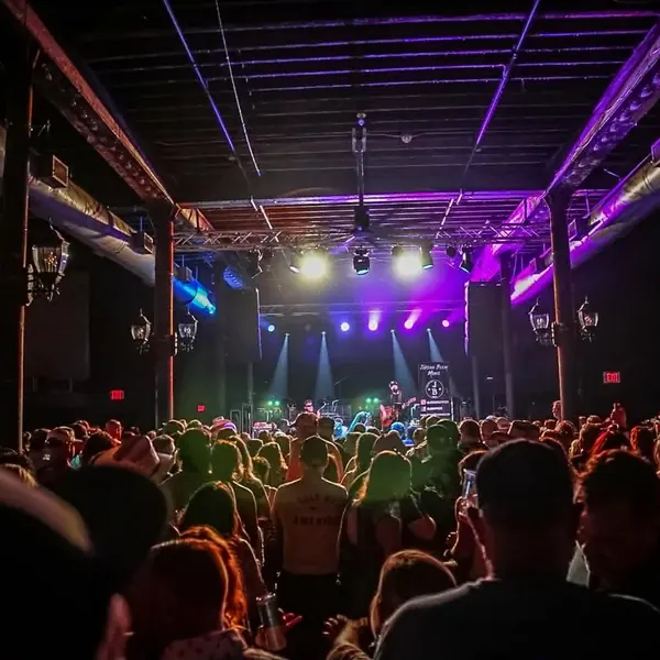 Crowd facing the stage in a ballroom venue lit in purple