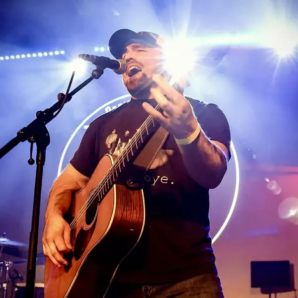 Jordan Beem singing into the microphone with acoustic guitar under bright stage lights