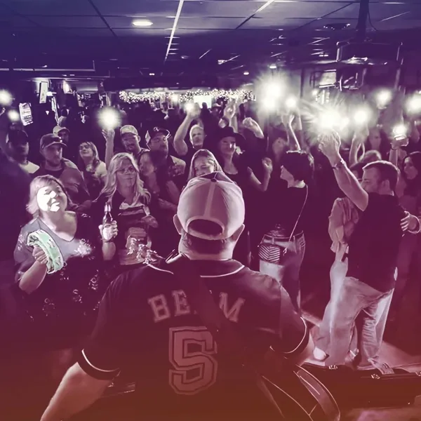 Jordan Beem on stage in his number 5 jersey, facing a packed bar crowd holding phone lights in the air